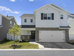 View of front of home featuring a porch, driveway, a garage, a front lawn, and stone siding