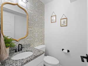 Half bath featuring vanity, baseboards, toilet, and wallpapered walls