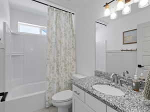 Bathroom with wainscoting, tile patterned flooring, vanity, toilet, and shower / tub combo