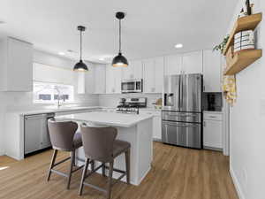 Kitchen with appliances with stainless steel finishes, light wood-type flooring, a sink, light countertops, and white cabinetry
