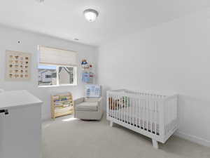 Carpeted bedroom featuring baseboards, a nursery area, and visible vents