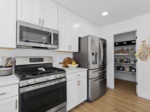 Kitchen with light countertops, white cabinetry, appliances with stainless steel finishes, and light wood-style flooring