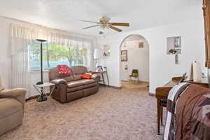 Carpeted living room featuring arched walkways, ceiling fan, baseboards, and a textured ceiling