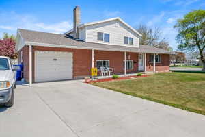 Traditional-style house with a porch, a chimney, a front yard, concrete driveway, and an attached garage