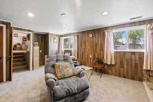 Carpeted living room featuring a textured ceiling, wood walls, and visible vents