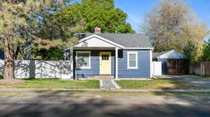 Bungalow featuring roof with shingles, fence, an outbuilding, and a chimney