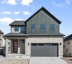 View of front of house with a shingled roof, an attached garage, concrete driveway, and stone siding