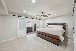 Bedroom with baseboards, a barn door, light carpet, and recessed lighting