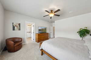 Bedroom with ensuite bathroom, ceiling fan, light carpet, and baseboards