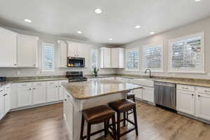 Kitchen featuring a sink, a center island, a breakfast bar, white cabinetry, and appliances with stainless steel finishes