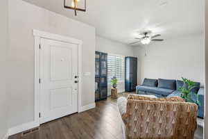 Living area with a ceiling fan, visible vents, wood finished floors, and baseboards