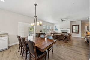 Dining room featuring ceiling fan with notable chandelier, baseboards, a lit fireplace, and light wood-type flooring