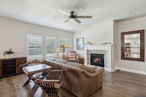 Living room with wood finished floors, a fireplace, baseboards, a ceiling fan, and a textured ceiling