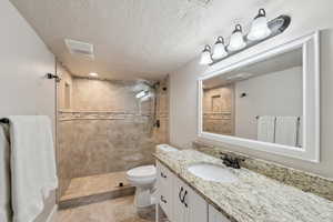 Bathroom featuring vanity, toilet, a tile shower, visible vents, and a textured ceiling