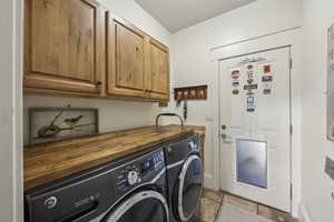 Clothes washing area with baseboards, cabinet space, stone finish floor, and washing machine and clothes dryer