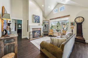 Living room featuring a tiled fireplace, high vaulted ceiling, baseboards, recessed lighting, and dark wood-type flooring