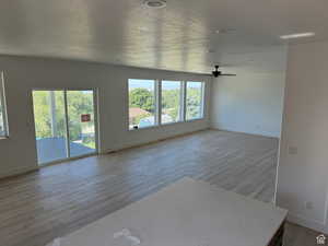 Unfurnished living room featuring baseboards, ceiling fan, a textured ceiling, and wood finished floors