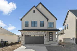 View of front of property with board and batten siding, an attached garage, driveway, and stone siding