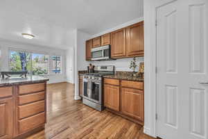 Kitchen featuring brown cabinets, light wood-type flooring, baseboards, dark stone countertops, and stainless steel appliances
