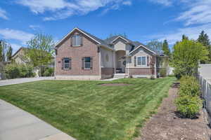 View of front of house with stucco siding, brick siding, fence, and a front lawn