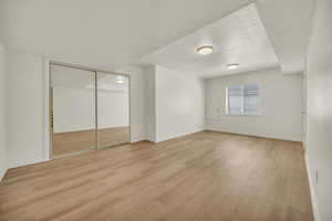 Unfurnished bedroom 6 featuring a textured ceiling, baseboards, light wood-style flooring, and a closet