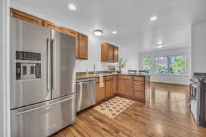 Kitchen featuring brown cabinetry, a sink, a peninsula, light wood-style floors, and stainless steel appliances