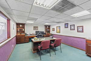 Carpeted office space with visible vents, a paneled ceiling, and baseboards