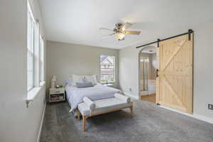 Carpeted bedroom featuring connected bathroom, ceiling fan, a barn door, arched walkways, and baseboards