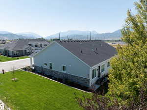 Exterior space with a lawn, a shingled roof, a mountain view, and stone siding