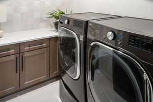 Clothes washing area featuring cabinet space, light tile patterned flooring, and washer and clothes dryer