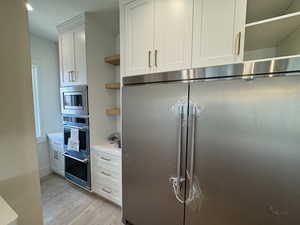 Kitchen featuring built in appliances, white cabinetry, open shelves, and light wood finished floors