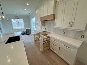 Kitchen with light stone countertops, light wood-style floors, recessed lighting, white cabinets, and a sink