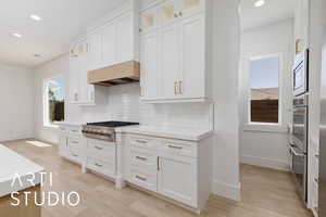 Kitchen with appliances with stainless steel finishes, baseboards, backsplash, white cabinets, and recessed lighting