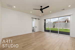 Spare room featuring a barn door, a ceiling fan, light wood-type flooring, baseboards, and recessed lighting