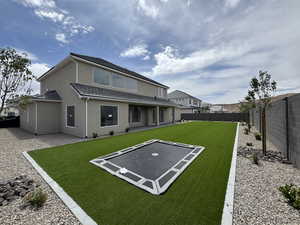 Rear view of property with a tiled roof, a trampoline, a fenced backyard, a yard, and stucco siding