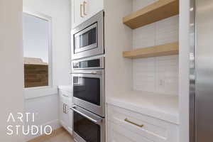 Kitchen with appliances with stainless steel finishes, decorative backsplash, light countertops, white cabinets, and open shelves