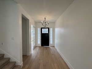 Entrance foyer with an inviting chandelier, baseboards, light wood finished floors, and stairs