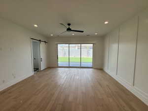 Empty room with baseboards, ceiling fan, light wood-type flooring, and a barn door