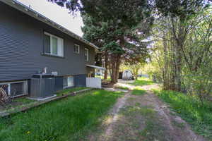 View of yard featuring dirt driveway, central AC, and fence