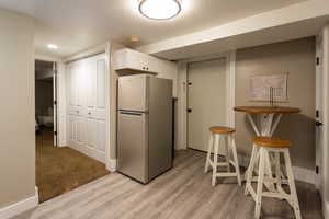 Kitchen featuring baseboards, freestanding refrigerator, light wood-type flooring, and white cabinetry
