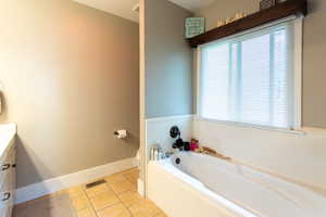 Bathroom featuring vanity, tile patterned flooring, a garden tub, toilet, and baseboards