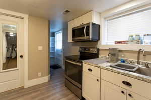 Kitchen featuring visible vents, wood finished floors, a sink, baseboards, and stainless steel appliances