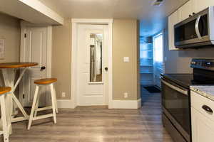 Kitchen with visible vents, wood finished floors, baseboards, white cabinets, and stainless steel appliances