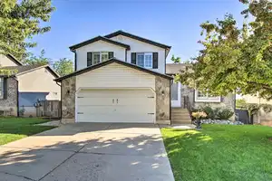 View of front of house with a front lawn, stone siding, concrete driveway, fence, and a garage