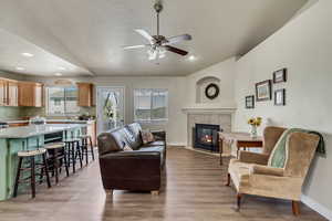 Living room featuring baseboards, a fireplace, vaulted ceiling, and light wood finished floors