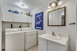 Laundry area with washer and dryer, a textured wall, laundry area, a sink, and a textured ceiling