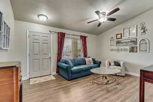 Living room featuring a ceiling fan, baseboards, wood finished floors, and a textured ceiling