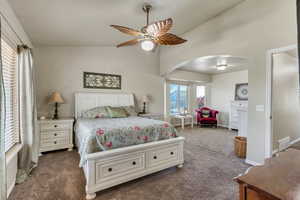 Carpeted bedroom with arched walkways, ceiling fan, and high vaulted ceiling