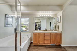 Full bath featuring double vanity, a sink, a garden tub, and wood finished floors