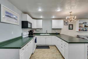 Kitchen with a peninsula, black microwave, dark countertops, white range with electric cooktop, and a sink